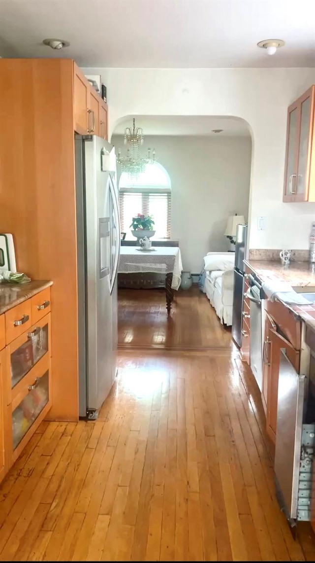 kitchen featuring appliances with stainless steel finishes, arched walkways, glass insert cabinets, and light wood finished floors