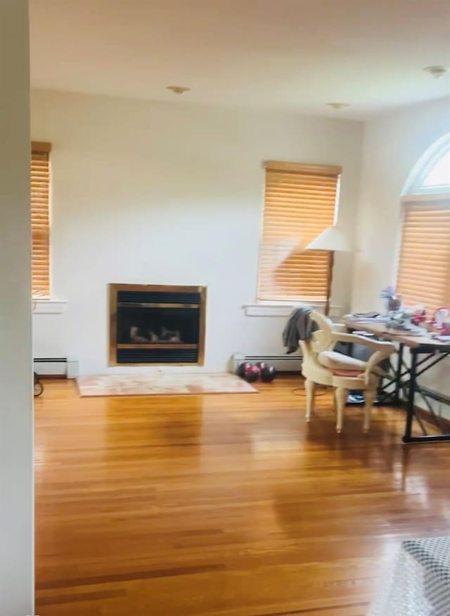 interior space with a baseboard heating unit, a glass covered fireplace, and wood finished floors