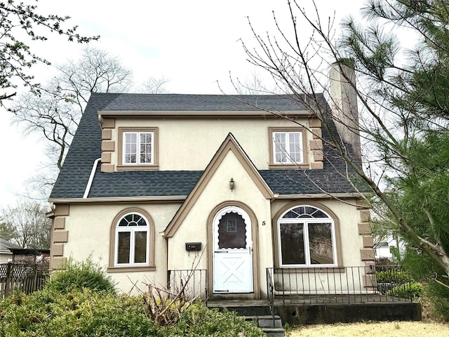 tudor home with stucco siding, fence, and a shingled roof
