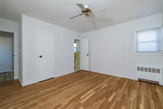 unfurnished bedroom with light wood-type flooring, radiator, crown molding, and baseboards