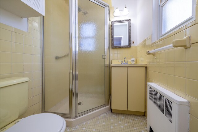 bathroom featuring a stall shower, toilet, radiator heating unit, vanity, and tile walls