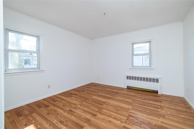 spare room featuring light wood-style floors, radiator heating unit, baseboards, and crown molding