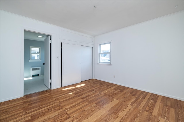 unfurnished bedroom featuring radiator, a closet, multiple windows, and wood finished floors