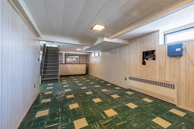 basement featuring tile patterned floors, wood walls, radiator heating unit, and stairs