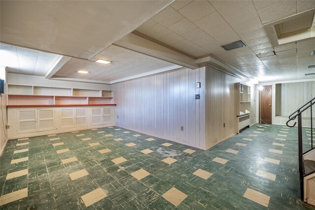 finished basement with wooden walls, stairway, and tile patterned floors