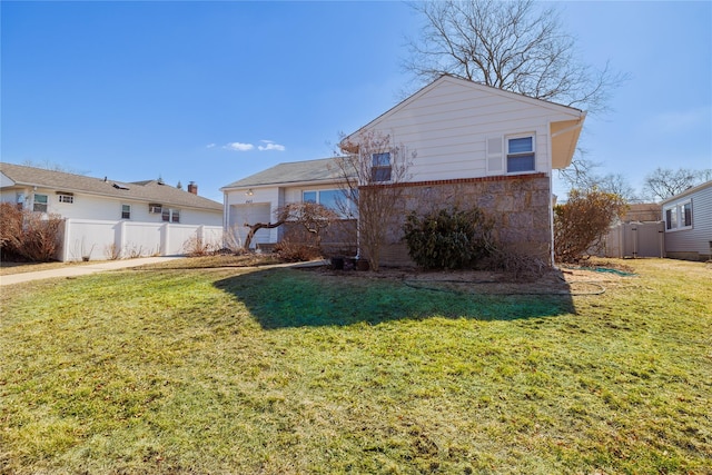 back of house featuring brick siding, a lawn, an attached garage, and fence