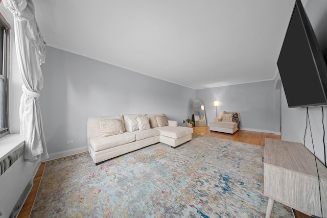 unfurnished living room with arched walkways, baseboards, radiator heating unit, and wood finished floors