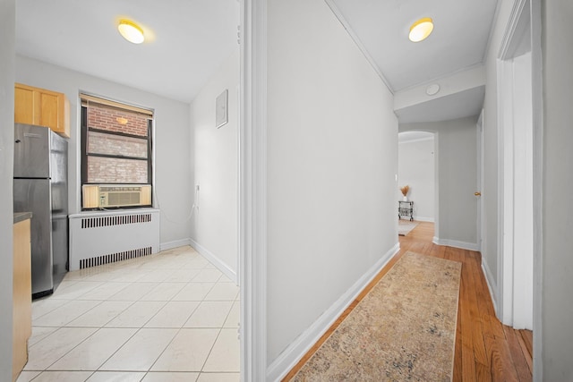 hallway featuring light tile patterned floors, arched walkways, baseboards, radiator heating unit, and cooling unit