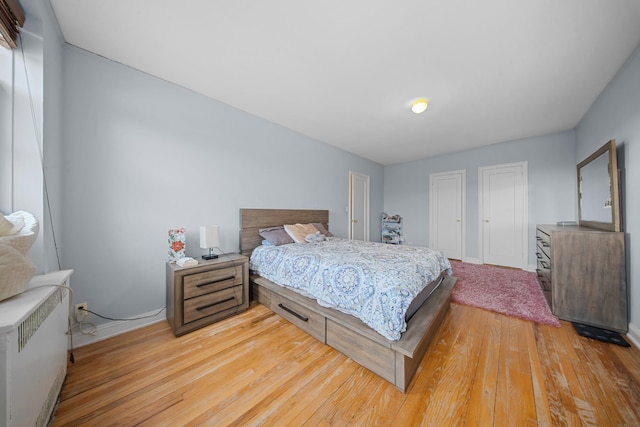 bedroom featuring radiator heating unit, light wood-type flooring, two closets, and baseboards