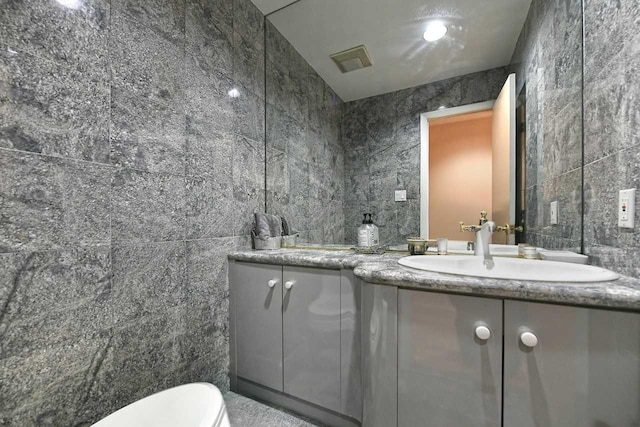 bathroom with tile walls, double vanity, visible vents, toilet, and a sink