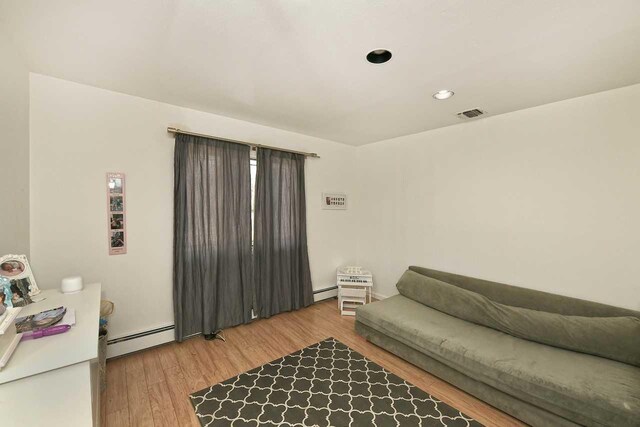 living room featuring a baseboard radiator, wood finished floors, visible vents, and recessed lighting