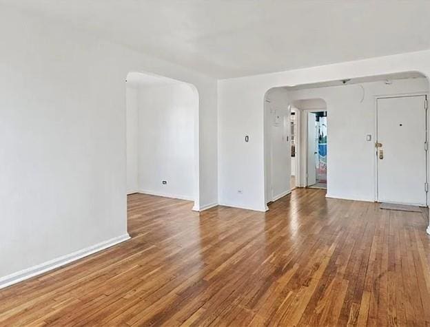 empty room featuring arched walkways and wood finished floors