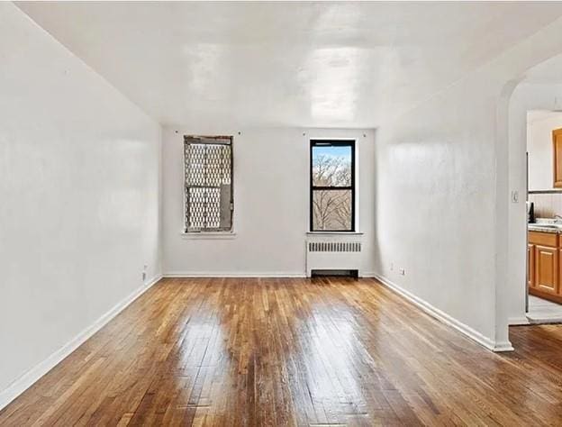 unfurnished room with arched walkways, radiator, baseboards, and hardwood / wood-style floors