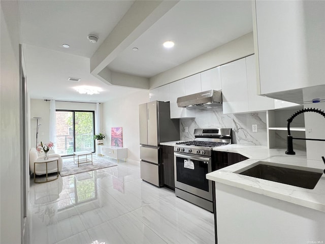 kitchen featuring white cabinets, light stone counters, stainless steel appliances, under cabinet range hood, and a sink