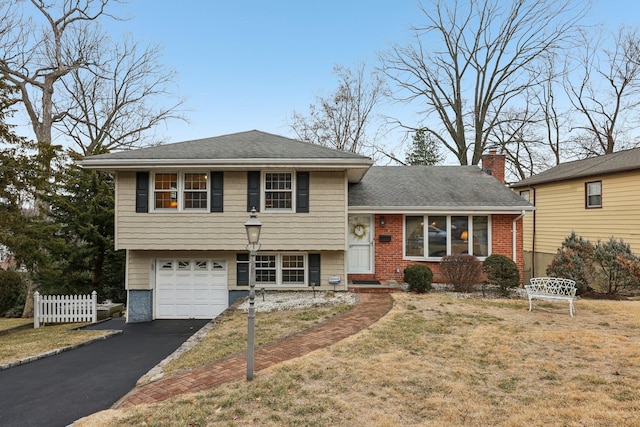 split level home with aphalt driveway, a chimney, fence, a garage, and a front lawn