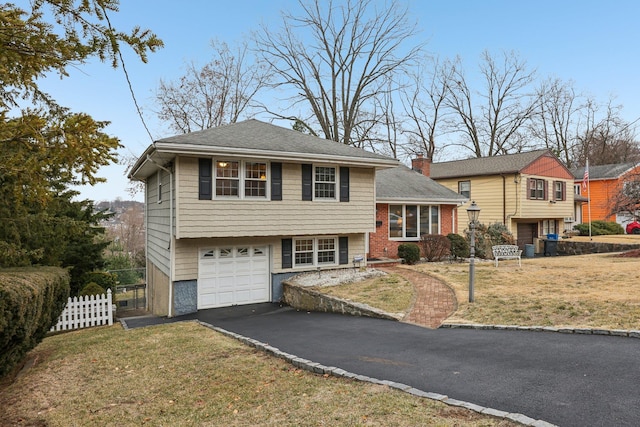 split level home with a garage, fence, driveway, a chimney, and a front yard