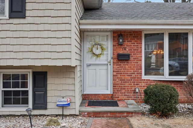 doorway to property featuring a shingled roof and brick siding