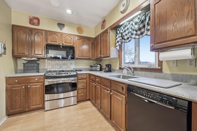 kitchen with a sink, light wood-style floors, light countertops, brown cabinets, and black appliances