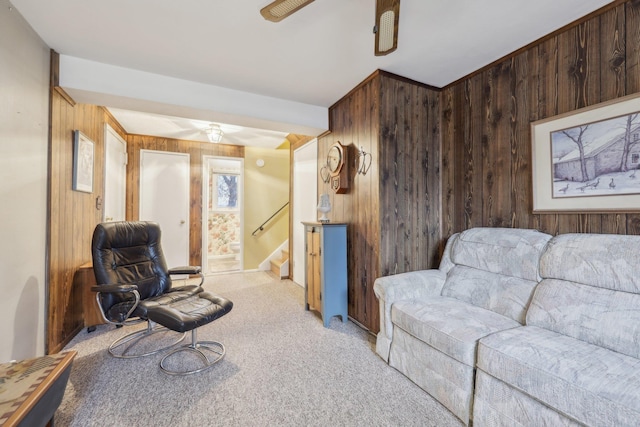 living room featuring stairway, wood walls, a ceiling fan, and light colored carpet