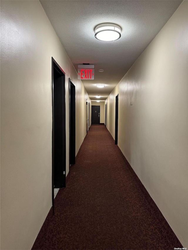 hallway featuring dark carpet and a textured ceiling