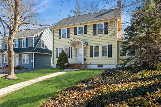 colonial home featuring entry steps, a chimney, and a front lawn