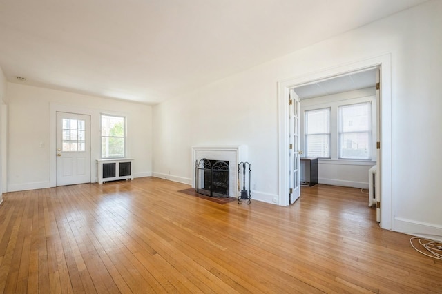 unfurnished living room with light wood-type flooring, a fireplace with flush hearth, and baseboards