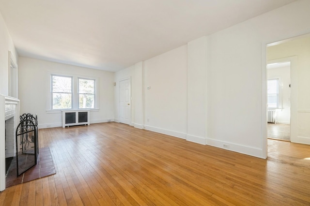 unfurnished living room featuring a brick fireplace, radiator heating unit, baseboards, and light wood finished floors