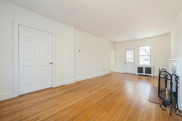 unfurnished living room featuring light wood finished floors, radiator heating unit, a fireplace, and baseboards