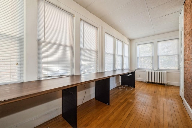 unfurnished office featuring radiator heating unit, built in study area, hardwood / wood-style flooring, and baseboards