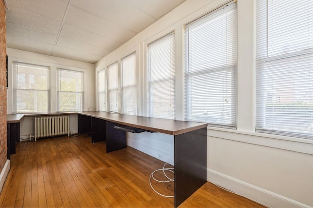 unfurnished office featuring built in desk, radiator heating unit, plenty of natural light, and hardwood / wood-style floors