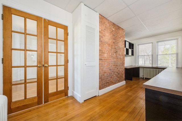 interior space featuring a drop ceiling, radiator, brick wall, wood-type flooring, and french doors