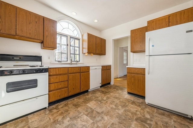 kitchen featuring brown cabinets, white appliances, light countertops, and a sink