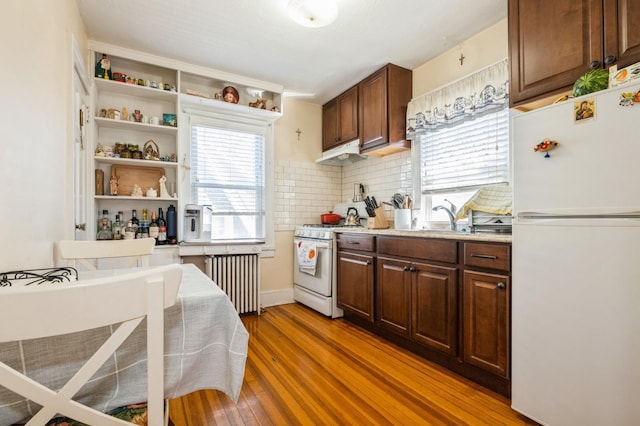 kitchen with decorative backsplash, radiator heating unit, light wood-type flooring, white appliances, and under cabinet range hood