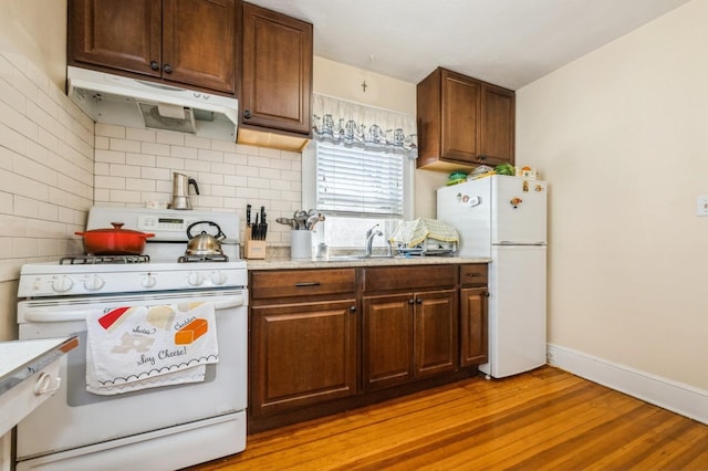 kitchen featuring white appliances, baseboards, light wood-type flooring, under cabinet range hood, and backsplash