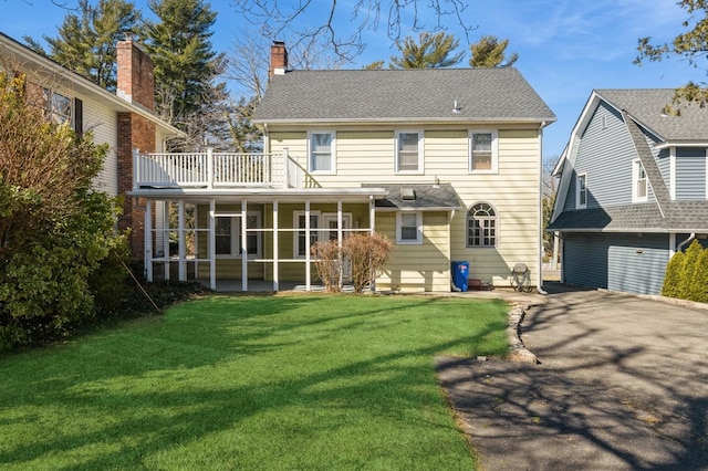 rear view of property with driveway, a shingled roof, a sunroom, a chimney, and a yard