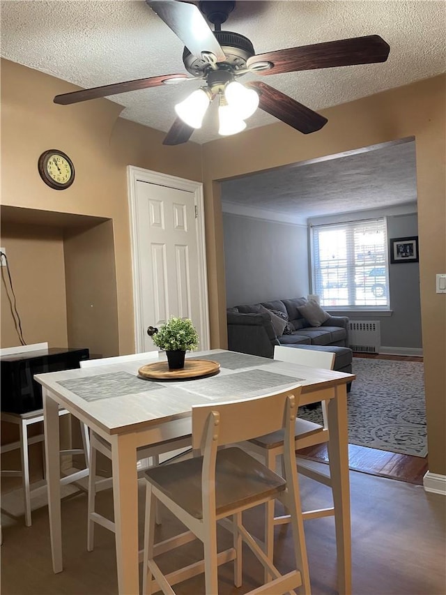 dining space with radiator, ceiling fan, a textured ceiling, and wood finished floors