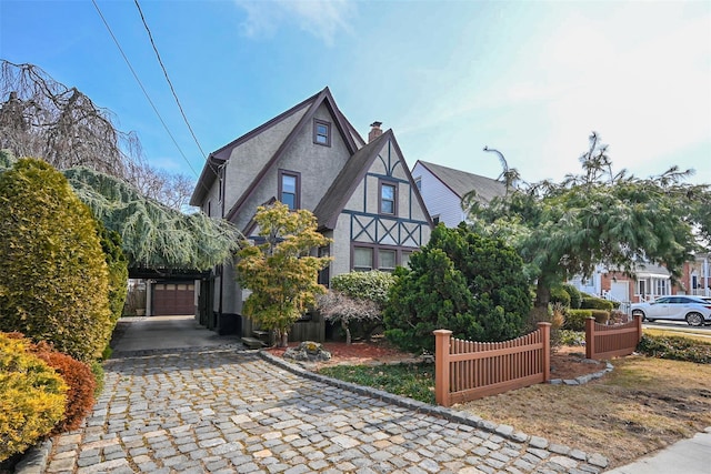 tudor-style house with a garage, fence, and stucco siding