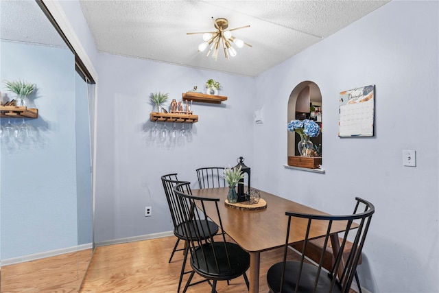 dining room featuring a textured ceiling, baseboards, wood finished floors, and a notable chandelier