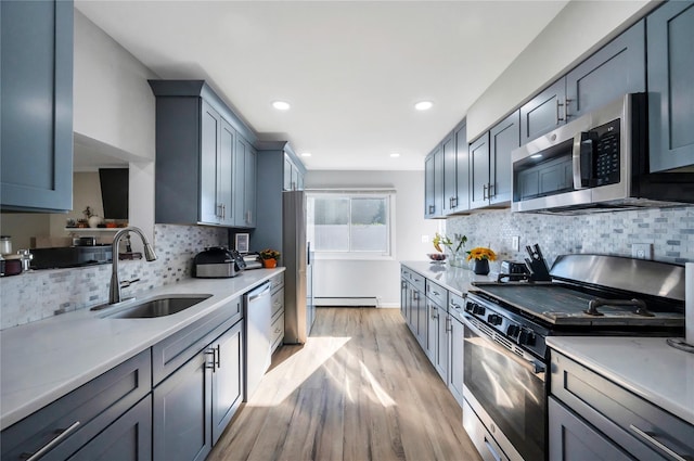 kitchen featuring light countertops, appliances with stainless steel finishes, light wood-style floors, a baseboard heating unit, and a sink