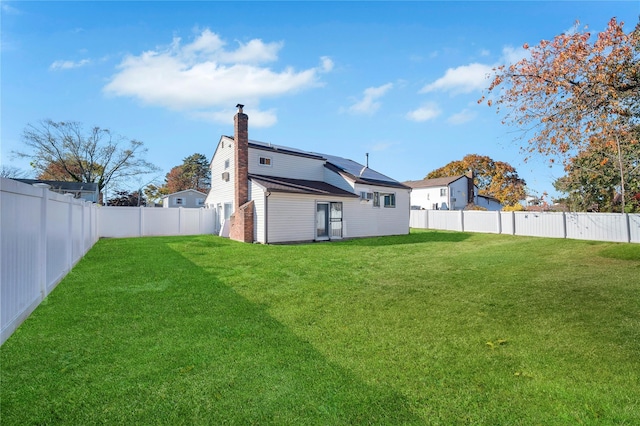 back of property featuring roof mounted solar panels, a fenced backyard, a yard, and a chimney