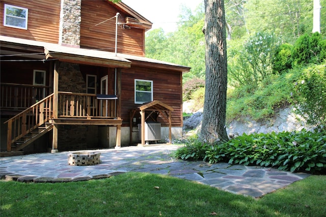 rear view of house featuring stone siding, an outdoor fire pit, stairs, and a patio