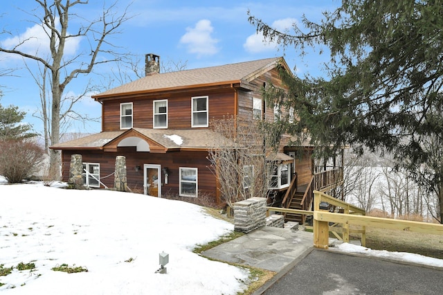 view of front facade with stairs, a chimney, and roof with shingles