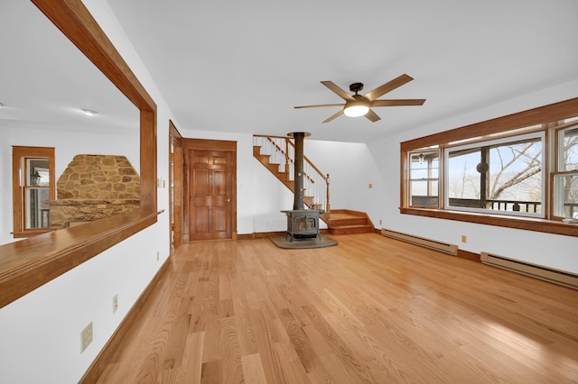 interior space with ceiling fan, a baseboard heating unit, wood finished floors, baseboards, and a wood stove