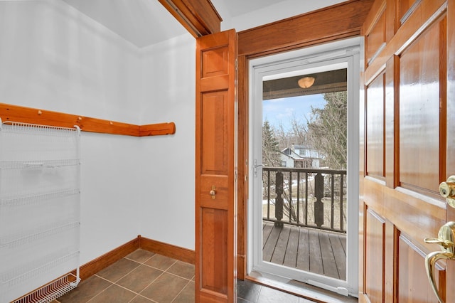 doorway with dark tile patterned flooring and baseboards