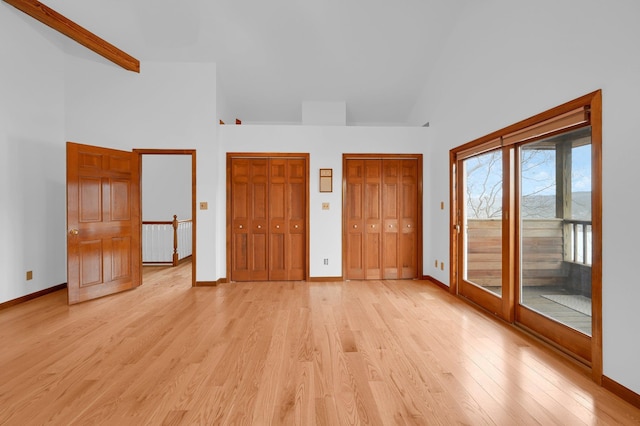 unfurnished bedroom featuring high vaulted ceiling, baseboards, access to outside, light wood finished floors, and two closets