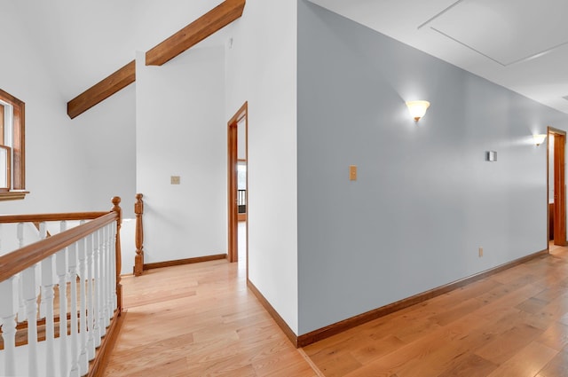 hallway featuring light wood-type flooring, lofted ceiling with beams, baseboards, and an upstairs landing