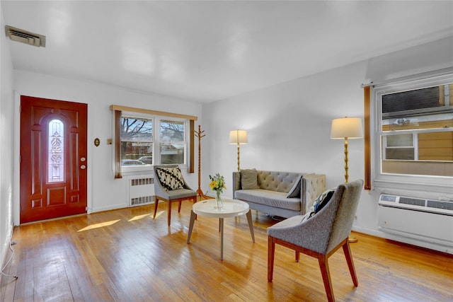 interior space with an AC wall unit, hardwood / wood-style flooring, visible vents, and radiator