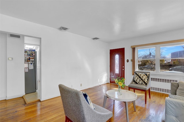 living room featuring light wood-style floors, radiator heating unit, and visible vents