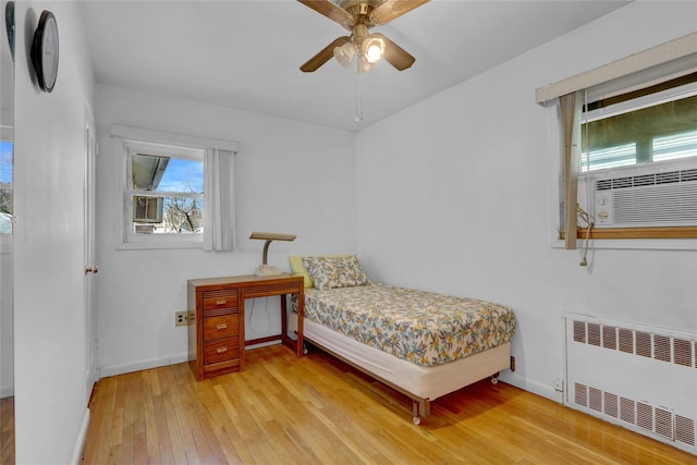 bedroom with cooling unit, light wood-style flooring, a ceiling fan, baseboards, and radiator