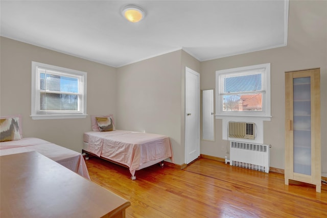 bedroom with radiator, light wood-style flooring, multiple windows, and baseboards